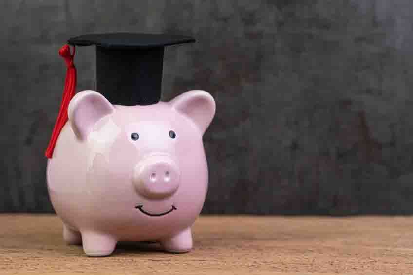 Smiling pink piggy bank wearing graduated hat on wooden table with dark black background and copy space, education fund, Scholarships, university cost and expense or saving for student loan concept